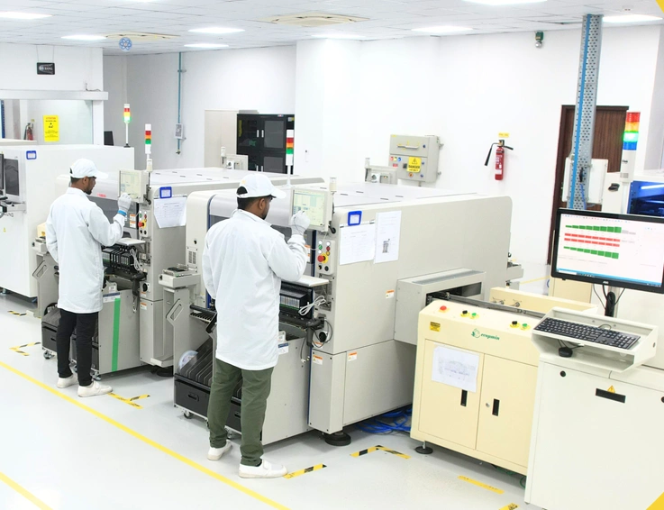 Technicians operating automated production machines in a cleanroom hardware manufacturing facility.